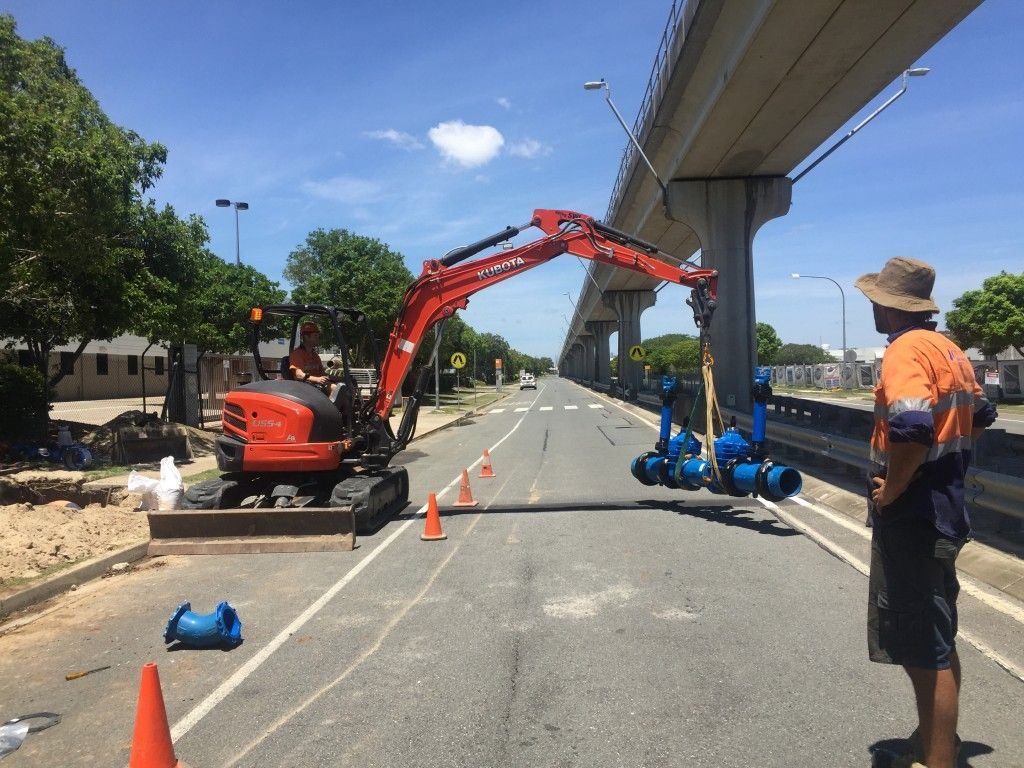 Excavator lifting a valve assembly into position on a live water main
